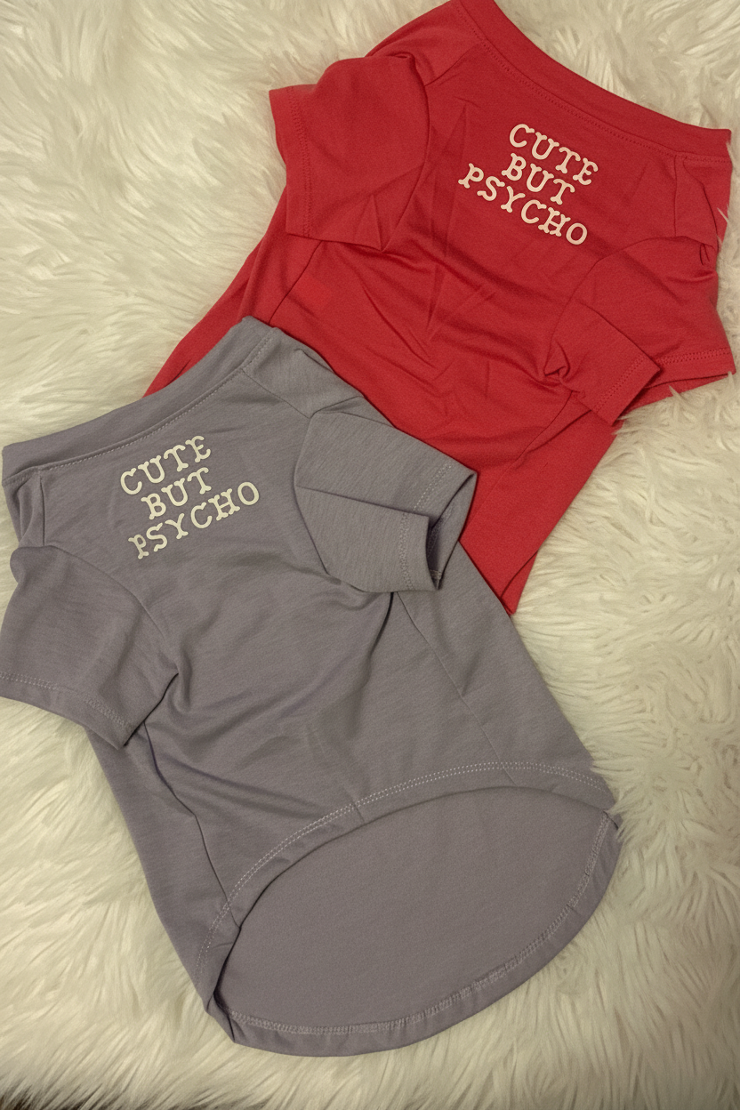 Two dog shirts, one gray and one red, with 'Cute But Psycho' text on a fluffy white surface.