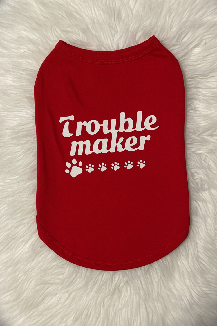 Red pet shirt with 'Trouble maker' text on a fluffy white surface